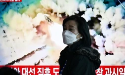 Une femme passe devant un écran de télévision diffusant des images d'archives d'un tir de missile nord-coréen, dans une gare de Séoul, le 18 mars 2024