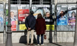 Des passants regardent les affiches électorales des candidats aux municipales à Paris le 9 mars 2026