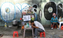 Un homme déjeune d'un bol de soupe aux nouilles sur l'étal d'une vendeuse de rue, le 8 septembre 2020 à Ho Chi Minh-Ville, au Vietnam
