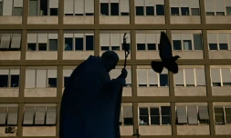 Un pigeon vole devant la statue du pape Jean-Paul II à l'extérieur de l'hôpital Gemelli où le pape François est hospitalisé pour une pneumonie, à Rome le 19 mars 2025