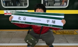 Un homme brandit une banderole "Pékin-Pyongyang" devant le train K27 à destination de Pyongyang, à la gare de Pékin, le 12 mars 2026 en Chine