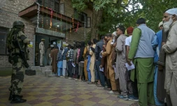 Un agent de sécurité indien monte la garde alors que les électeurs font la queue pour voter dans un bureau de vote lors de la première phase des élections législatives à Pulwama, au sud de Srinagar, le 18 septembre 2024