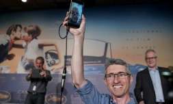 Le cinéaste Fabrice Aragno brandit un téléphone portable où l'on voit le réalisateur franco-suisse Jean-Luc Godard donner une conférence de presse par visio-conférence depuis la Suisse, le 12 mai 2018 à Cannes