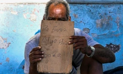 Un homme tient un morceau de carton sur lequel est écrit "S'il vous plaît, pour manger", alors qu'il mendie dans une rue de La Havane, le 21 juillet 2025 à Cuba