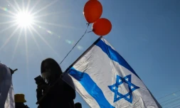 Des Israéliens portant le drapeau national et des ballons orange attendent l'arrivée du convoi funéraire de la famille Bibas, dans le kibboutz Nir Oz, dans le sud d'Israël, le 26 février 2025