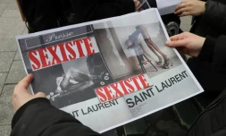 Une personne montre deux reproductions des affiches Saint Laurent, lors d'une manifestation à Paris le 7 mars 2017. Jugées "dégradantes" pour l'image de la femme, ces images ont finalement été retirées