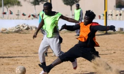 Des migrants Camerounais (orange) et Sénégalais (jaune) participent à un match de football au camp de Tarjoura en Libye, le 28 février 2018