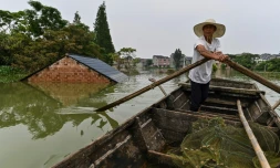 Un pĂȘcheur passe en barque prĂšs d'une habitation dont n'Ă©merge que le toit, dans le village de Longkou, dans la rĂ©gion de Poyang qui a subi des pluies violentes, dans la province du Jiangxi, au centre de la Chine, le 16 juillet 2020