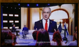 Cette photo prise sur un écran de TF1, montre le président français Emmanuel Macron, alors qu'une photo du Premier ministre israélien Benjamin Netanyahu s'affiche en arrière-plan, lors d'une émission dans les studios de télévision de Saint-Denis, le 13 mai 2025