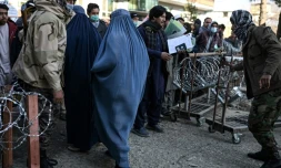 Deux femmes en burqa quittent le bureau des passeport dont l'entrée est contrôlée par des talibans, le 18 décembre 2021 à Kaboul