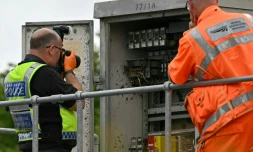 Un membre de la police des transports britannique photographie l'intérieur d'un boîtier de localisation (LOC) en bordure de voie, près du site d'une collision entre deux trains de l'East Midlands Railway (EMR) survenue la veille, le 20 juin 2026 au sud de Bedford, dans le centre de l'Angleterre