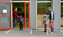 Un enseignant portant un masque de protection accueille un enfant dans sa classe tandis qu'un autre attend Ă distance, le 12 mai 2020 Ă l'Ă©cole publique Champ l'EvĂȘque de Bruz