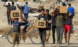 Des Palestiniens portent des cartons d'aide humanitaire reçus dans un centre de distribution géré par la Fondation humanitaire de Gaza (GHF), alors qu'ils traversent le "corridor de Netzarim", dans le centre de la bande de Gaza, le 22 août 2025