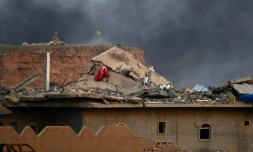 Cette photo prise le 22 mars 2019 montre un toit endommagé et une fumée noire s'élevant du village de Baghouz en Syrie avec des drapeaux de forces kurdes levés 