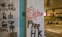 Un graffiti sur un mur aprÚs des affrontements entre des manifestants et des policiers anti-émeutes qui se reposent à l'arriÚre-plan (D), à Hong Kong au petit matin du 22 juillet 2019