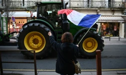 Un agriculteur manifeste avec son tracteur, salué par une passante avec un drapeau français, à Agen, dans le Lot-et-Garonne, le 25 janvier 2024