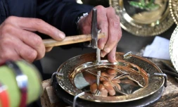 Un artisan grave un dessin sur une plaque de cuivre dans sa boutique des souks de la médina de Tunis, le 7 décembre 2023