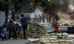 Un manifestant jette un projectile en direction des forces de l'ordre alors que d'autres se protègent derrière une barricade, protestant contre le coup d'Etat militaire, le 17 mars 2021 à Rangoun