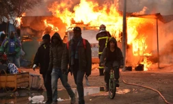 De jeunes migrants quittent la "Jungle" de Calais où un pompier tente d'éteindre un feu, le 26 octobre 2016