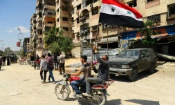 Photo fournie par l'agence de presse syrienne officielle Sana montrant un homme à moto tenant le drapeau syrien dans une rue de Douma, le 14 avril 2018