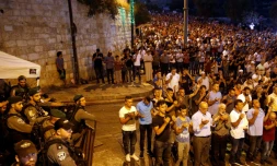 Des forces de sécurité israéliennes regardent des Palestiniens prier à l'extérieur de l'esplanade des Mosquées à Jérusalem, le 24 juillet 2017