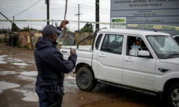 Un policier sud-africain soulÚve la bande jaune barrant l'accÚs pour permettre à un expert de la police scientifique d'approcher la scÚne d'une tuerie dans un bar clandestin, le 21 décembre 2025 à Bekkersdal (Afrique du Sud)