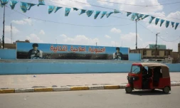 Un "touk-touk" passe devant une affiche à la gloire du leader chiite Moqtada Sadr dans une rue du quartier pauvre de Sadr City à Bagdad, le 14 mai 2018