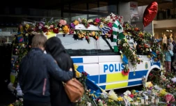 Des personnes se recueillent devant un véhicule de police recouvert de fleurs sur le site d'un attentat au camion-bélier, le 10 avril 2018 à Stockholm