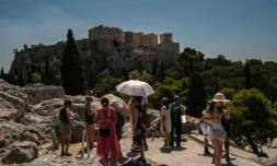 Des touristes se protègent du soleil en face de la colline de l'Acropole à Athènes, le 8 juillet 2025 en Grèce