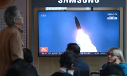 Des personnes sont assises devant un écran de télévision diffusant un journal télévisé avec des images d'archives d'un test de missile nord-coréen, dans une gare de Séoul, le 22 octobre 2025