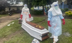 Des membres du personnel médical, en combinaisons de protection, près du cercueil d'un patient décédé du virus Ebola dans un hôpital à Rwampara, le 21 mai 2026 en RDC