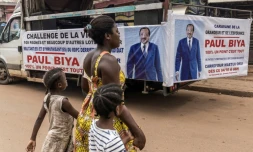 Une femme et ses enfants traversent la rue près d'un camion de campagne du président sortant du Cameroun, Paul Biya, à Yaoundé le 11 octobre 2025