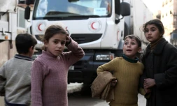 Des enfants syriens devant un convoi d'aide humanitaire du croissant rouge à Kafr Batna, dans les environs de Damas, le 23 février 2016