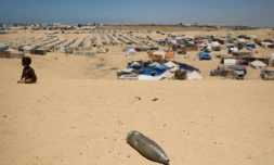 Un obus non explosé non loin d'un enfant assis sur le sable près d'un camp de fortune pour Palestiniens déplacés dans la zone de Tel al-Sultan à Rafah, dans le sud de la bande de Gaza, le 30 mai 2024