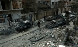 Photo prise le 25 février 2018 montrant un homme marchant dans une rue de la ville de Douma au milieu de voitures détruites et immeubles endommagés après des raids aériens du régime syrien sur la Ghouta orientale, une enclave rebelle près de Damas bombardée par le régime syrien