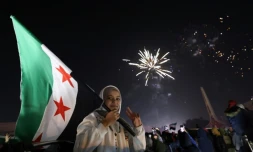 Une jeune femme tient le drapeau de la Syrie devant une foule célèbrant le Nouvel An près de la place des Omeyyades à Damas, en Syrie, le 1er janvier 2025