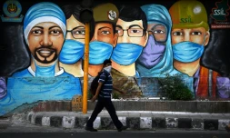 Un homme passe devant une fresque de rue représentant des personnels luttant contre le coronavirus, le 14 juillet 2020 à New Delhi