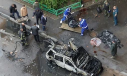 Des membres des forces de l'ordre et des services funéraires russes à cÎté d'une voiture détruite par un engin explosif à  Balachikha, à l'est de Moscou, le 25 avril 2025