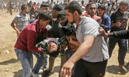 Un Palestinien blessé par des tirs israéliens est évacué par d'autres manifestants, le 14 mai 2018 dans la bande de Gaza, à la frontière avec Israël