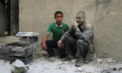 Deux hommes assis dans une rue après un raid aérien attribué aux troupes du régime dans le quartier de Sukkari, sous contrôle rebelle, à Alep, le 30 mai 2016 