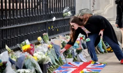 Une femme dépose un bouquet de fleurs en hommage au prince Philip devant les grilles du palais de Buckingham, à Londres, le 9 avril 2021.