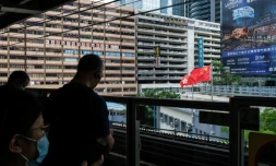 Des voyageurs sur le quai d'une station de métro à Hong Kong, avec le drapeau chinois en arriÚre-plan, le 29 mai 2020