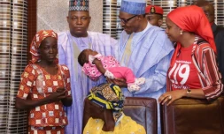 Le président du Nigeria Mohammadu Buhari (c) tient dans ses bras l'enfant d'Amina Ali (g), la premiÚre des 219 lycéennes de Chibok kidnappées par Boko Haram à avoir été retrouvée, le 19 mai 2016 à Maiduguri