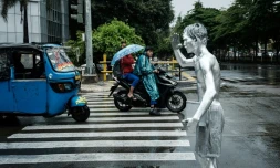 L'artiste de rue Ari Munandar (d), le corps recouvert de peinture argentée, fait la manche sous la pluie à un carrefour de Jakarta, le 1er avril 2025 en Indonésie
