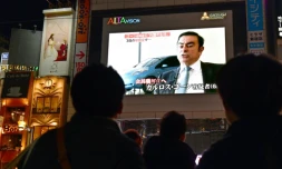 Des passants regardent le 22 novembre 2018 Ă Tokyo la photo de Carlos Ghosn, patron de Renault-Nissan, arrĂȘtĂ© pour soupçons de malversations financiĂšres et fraude fiscale