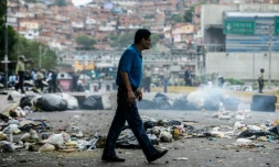 Un homme traverse une route barrée par des sacs poubelles, le 2 mai 2017 à Caracas