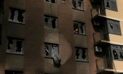 Un homme à travers une vitre brisée à l'intérieur d'un immeuble résidentiel endommagé par des frappes russes, à Kiev en Ukraine le 14 mai 2026