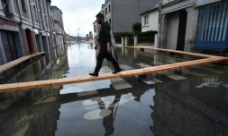 Un homme marche sur des planches surélevées pour circuler dans une rue inondée de Redon, le 30 janvier 2025, en Ille-et-Vilaine