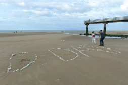Une famille sur "Omaha Beach", où le mot "D-Day" a été tracé à l'aide de galets, à  Vierville-sur-Mer, dans le Calvados, lors des célébrations du 75e anniversaire du Débarquement en juin 2019