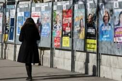 Une femme passe devant un panneau électoral avec les candidats à la mairie de Paris, le 9 mars 2026, à Paris